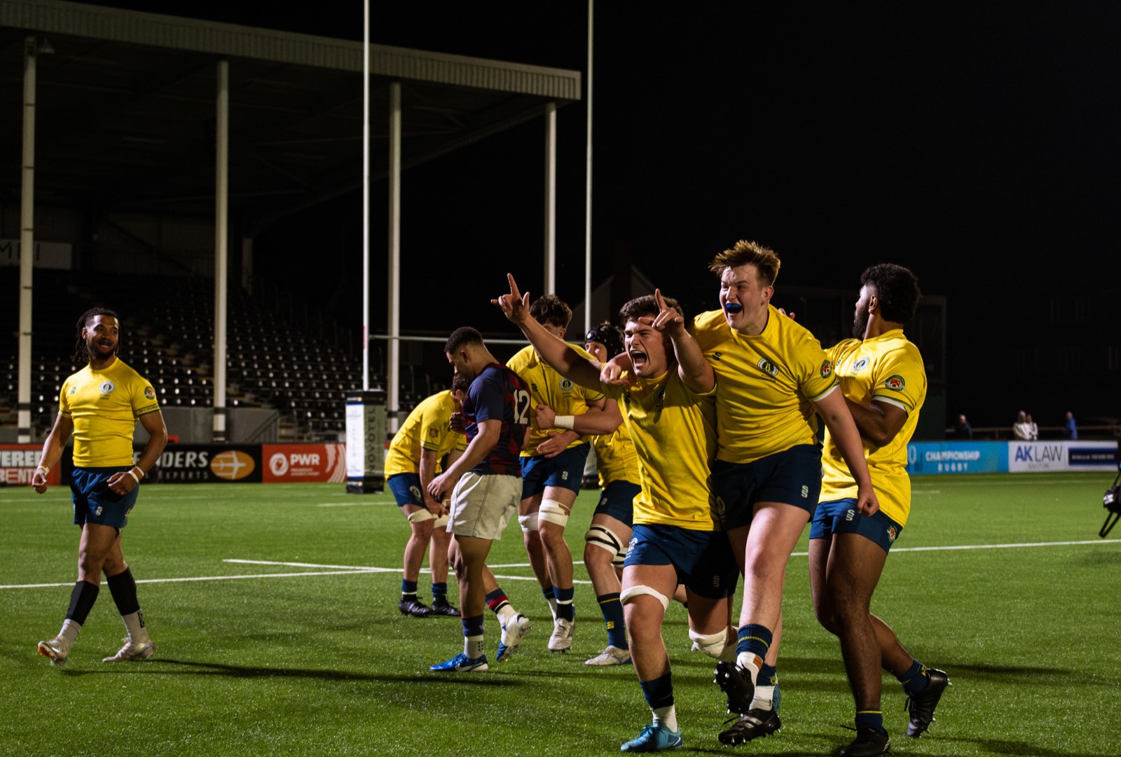 Rugby players celebrating a try under floodlights